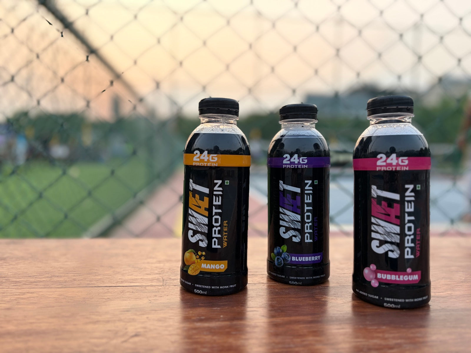 Three SWÆT bottles at sunset against a court fence